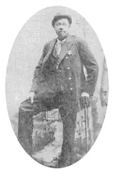 Ansel Clarke photo. Man wearing overcoat, long slacks, and an officers uniform from the late 1800s to early 1900s. Fedora style round hat.