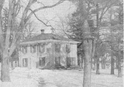 Black and white phot of a two story stone home in a wooded area