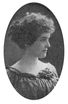 Young woman in mid 20s with curly hair pulled back into a bun. Blouse without shoulders.